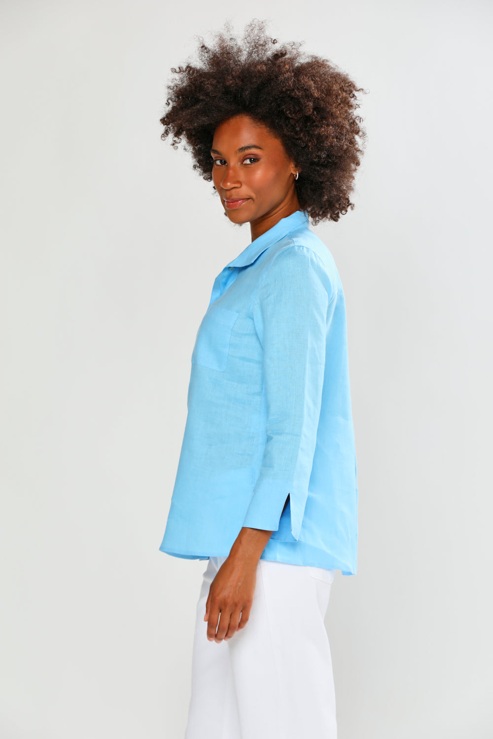 Woman wearing a light blue shirt and white pants on a plain background