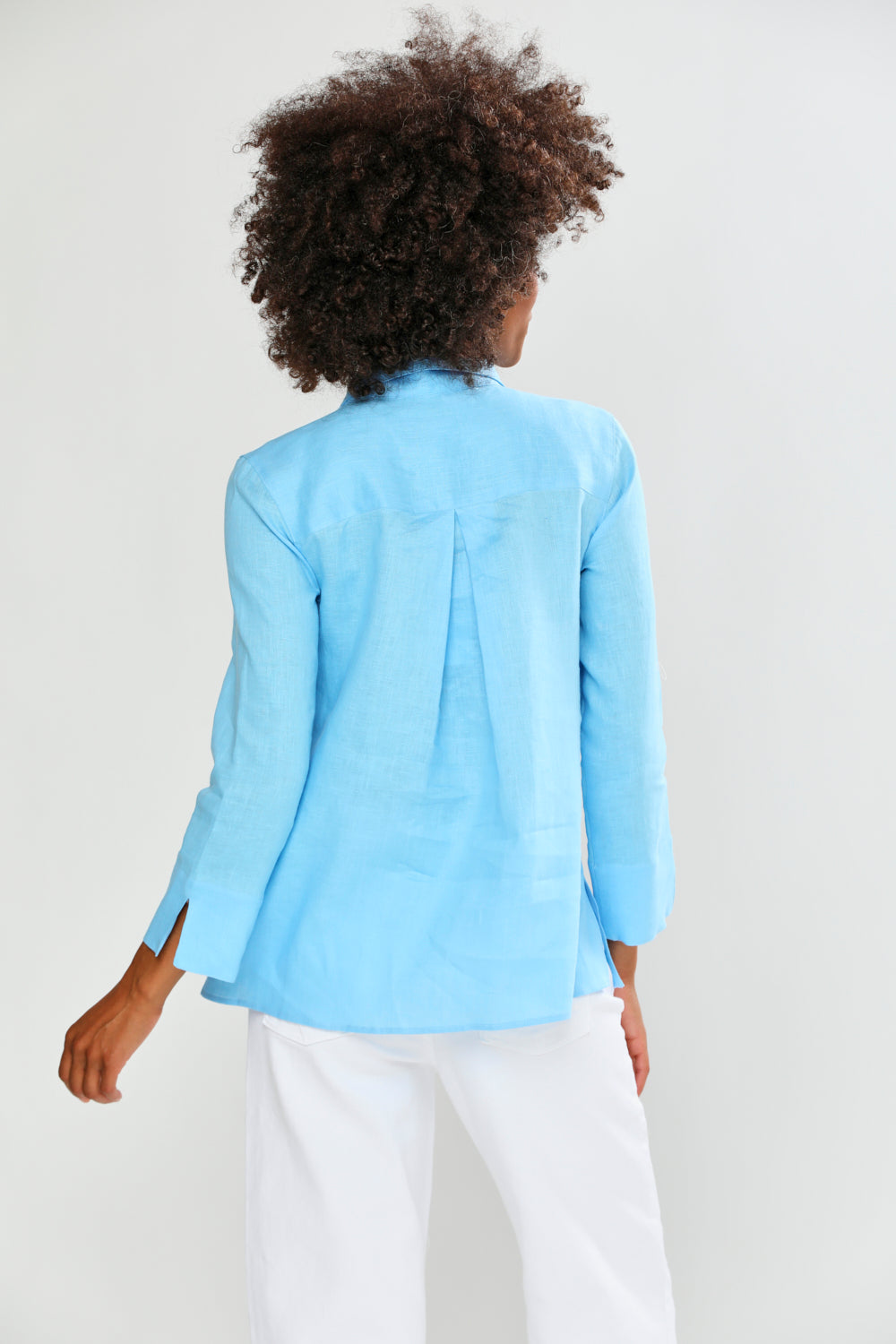 Person wearing a light blue shirt and white pants on a plain background