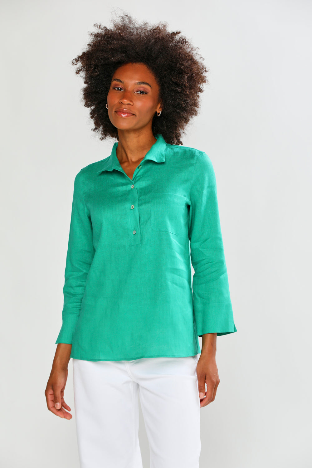 Woman wearing a green shirt and white pants against a plain background