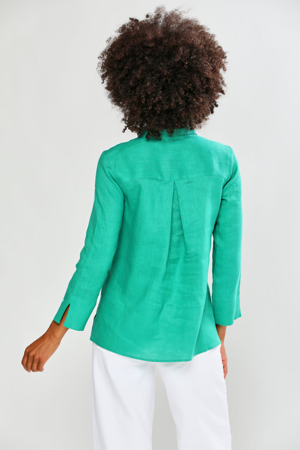 Person wearing a green blouse  and white pants on a plain background