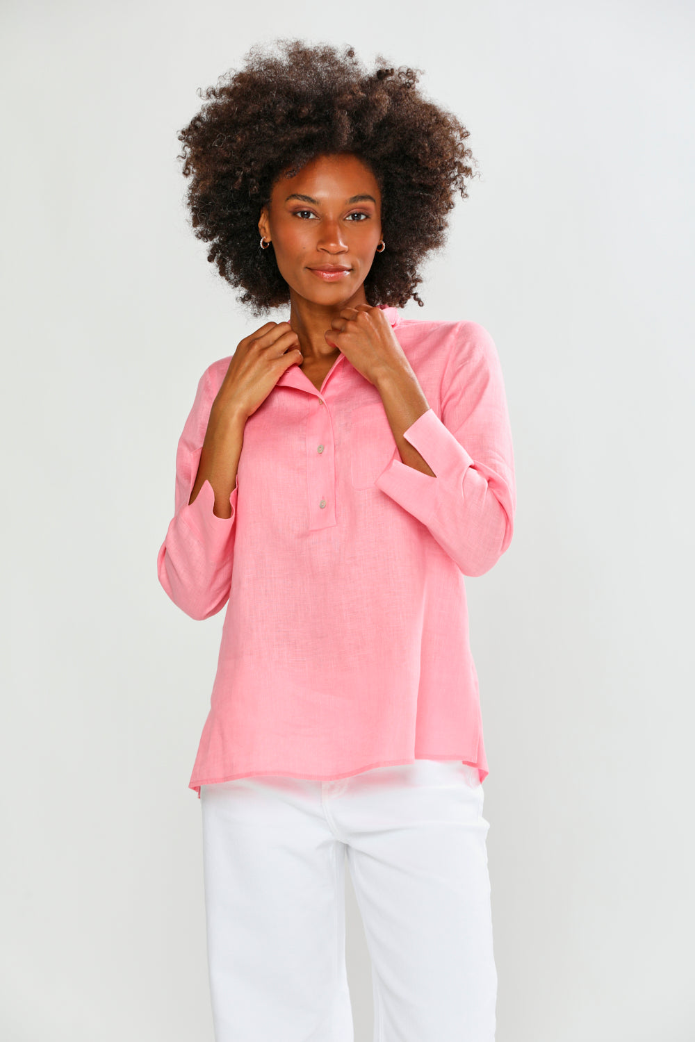 Woman wearing a pink blouse and white pants against a plain background