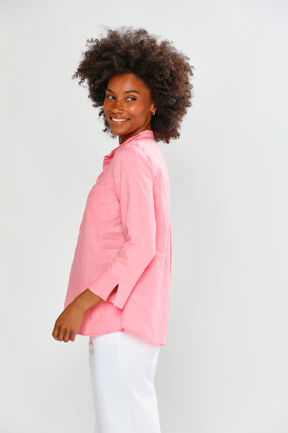 Woman wearing a pink shirt and white pants on a plain background