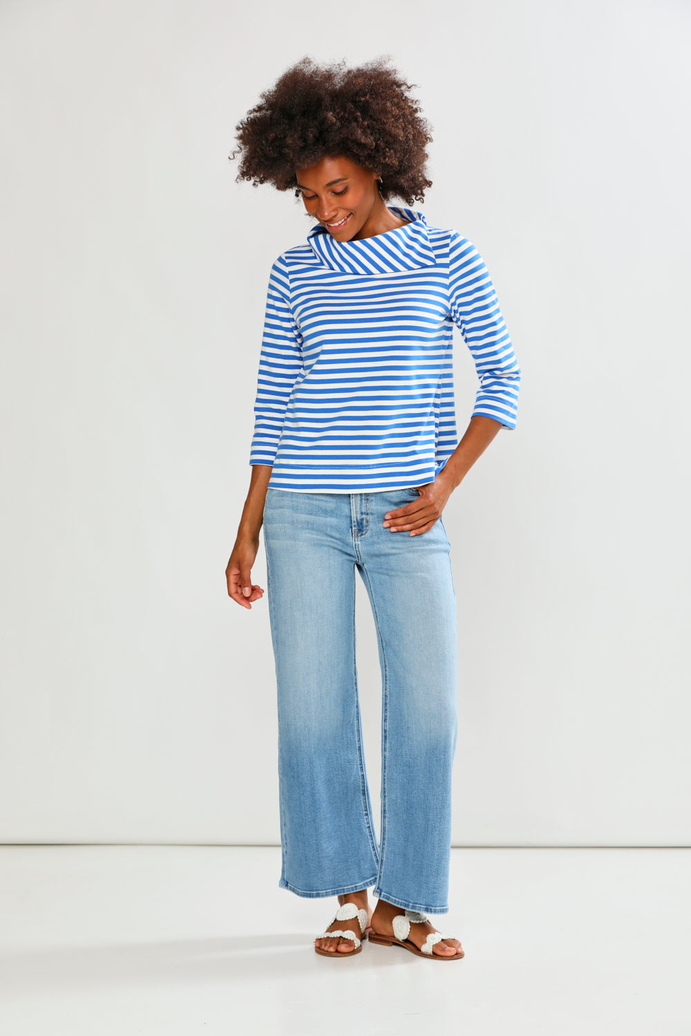 Woman wearing a blue and white striped shirt and light blue jeans on a white background