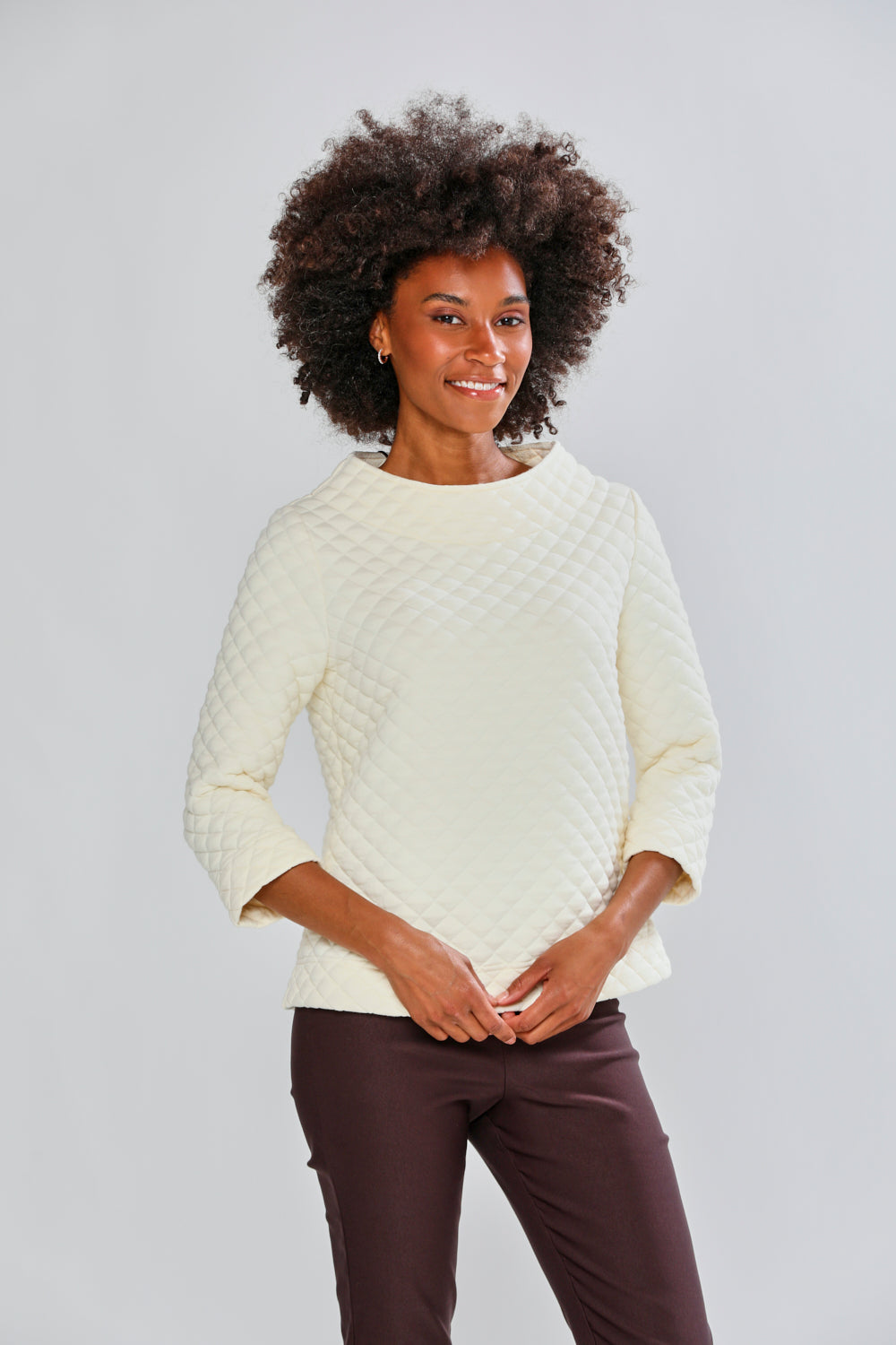 Woman wearing a cream sweater and brown pants against a light gray background