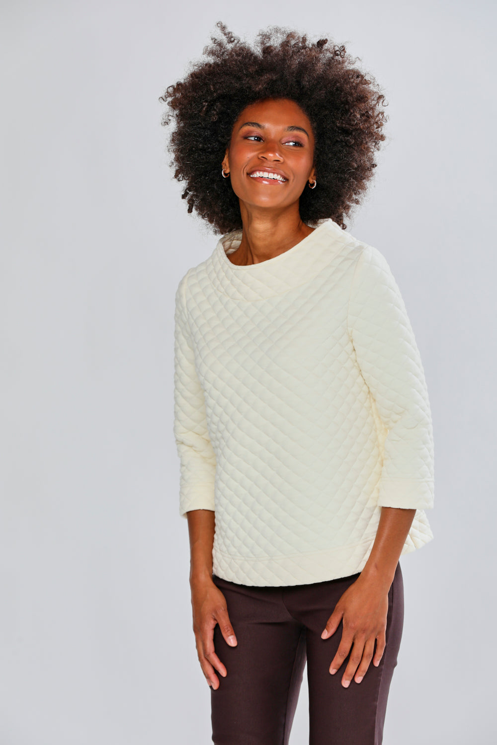 Woman wearing a cream sweater and brown pants against a light gray background