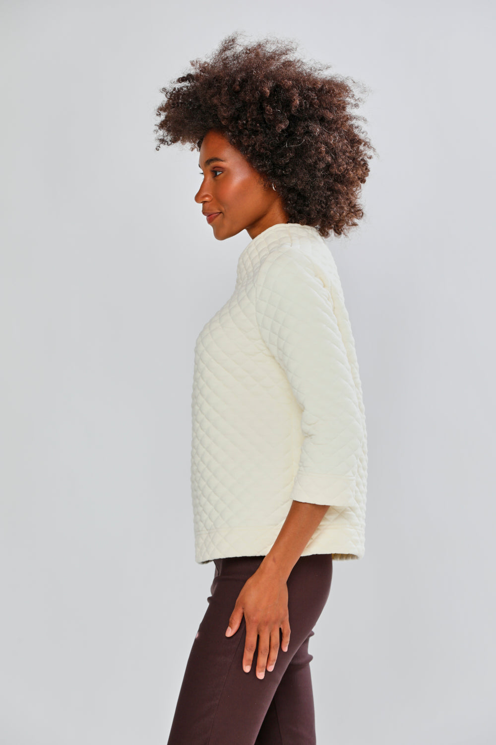 Woman wearing a cream sweater and brown pants against a light gray background