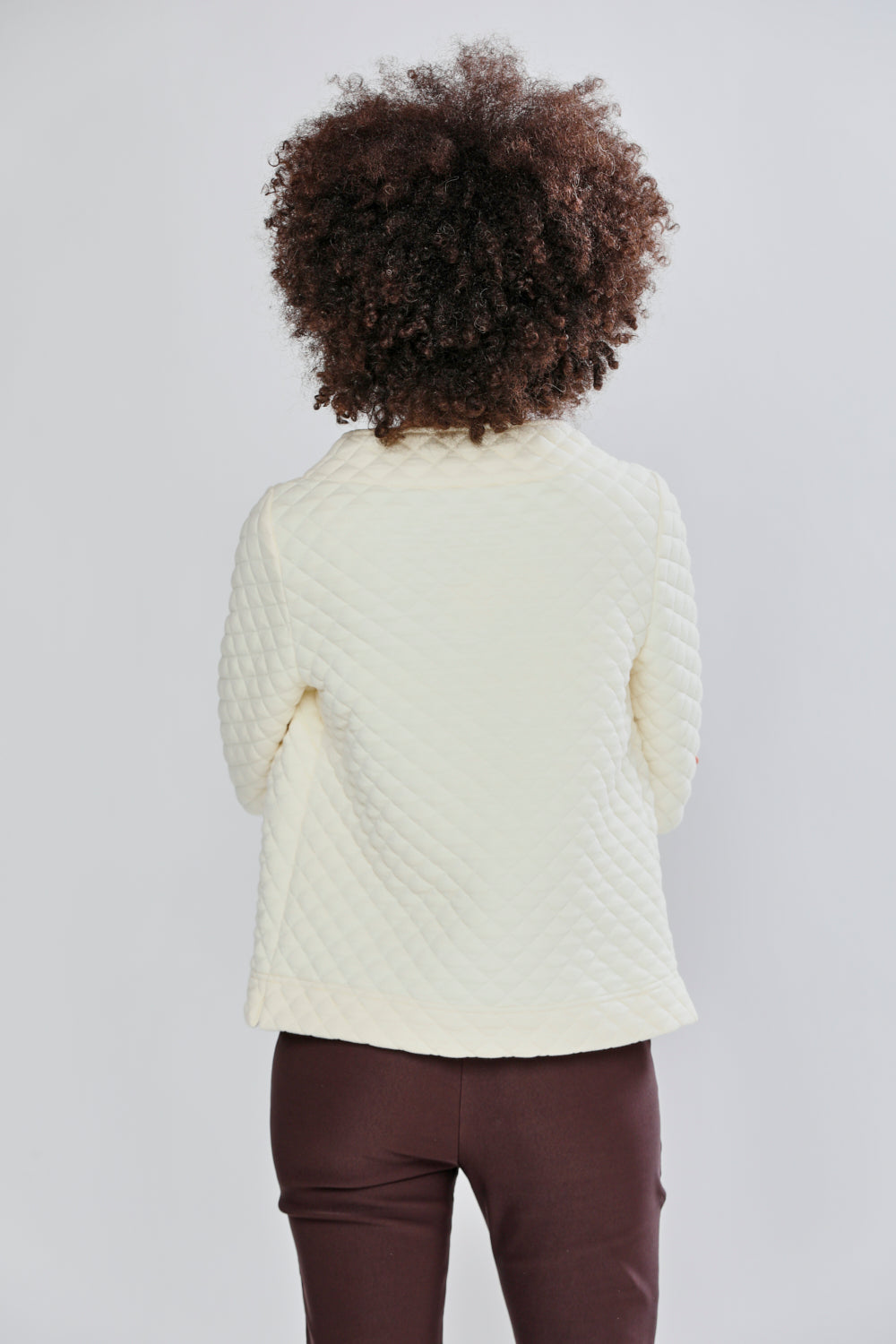 Woman wearing a cream sweater and brown pants against a light gray background