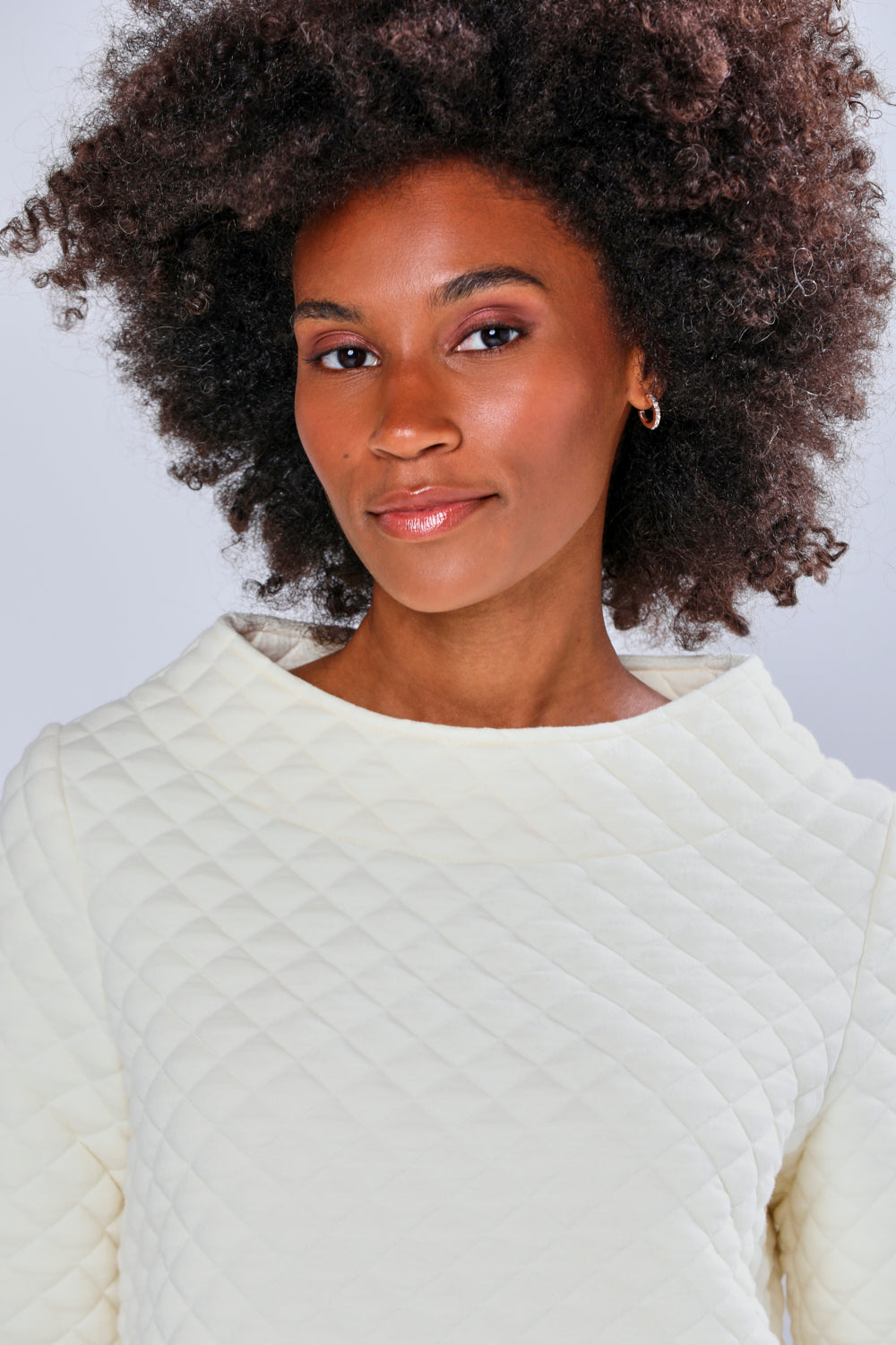 Woman wearing a cream sweater and brown pants against a light gray background
