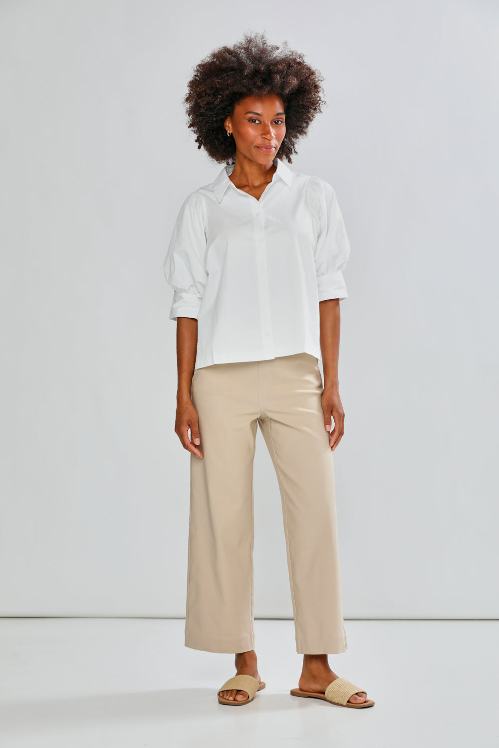 Woman wearing a white shirt and beige pants against a white background
