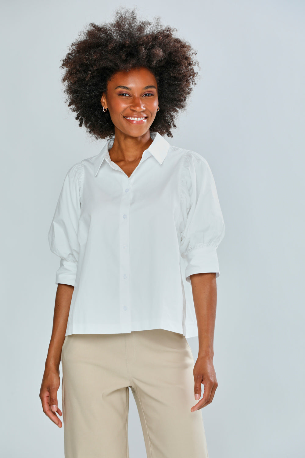 Woman wearing a white shirt and beige pants against a light gray background