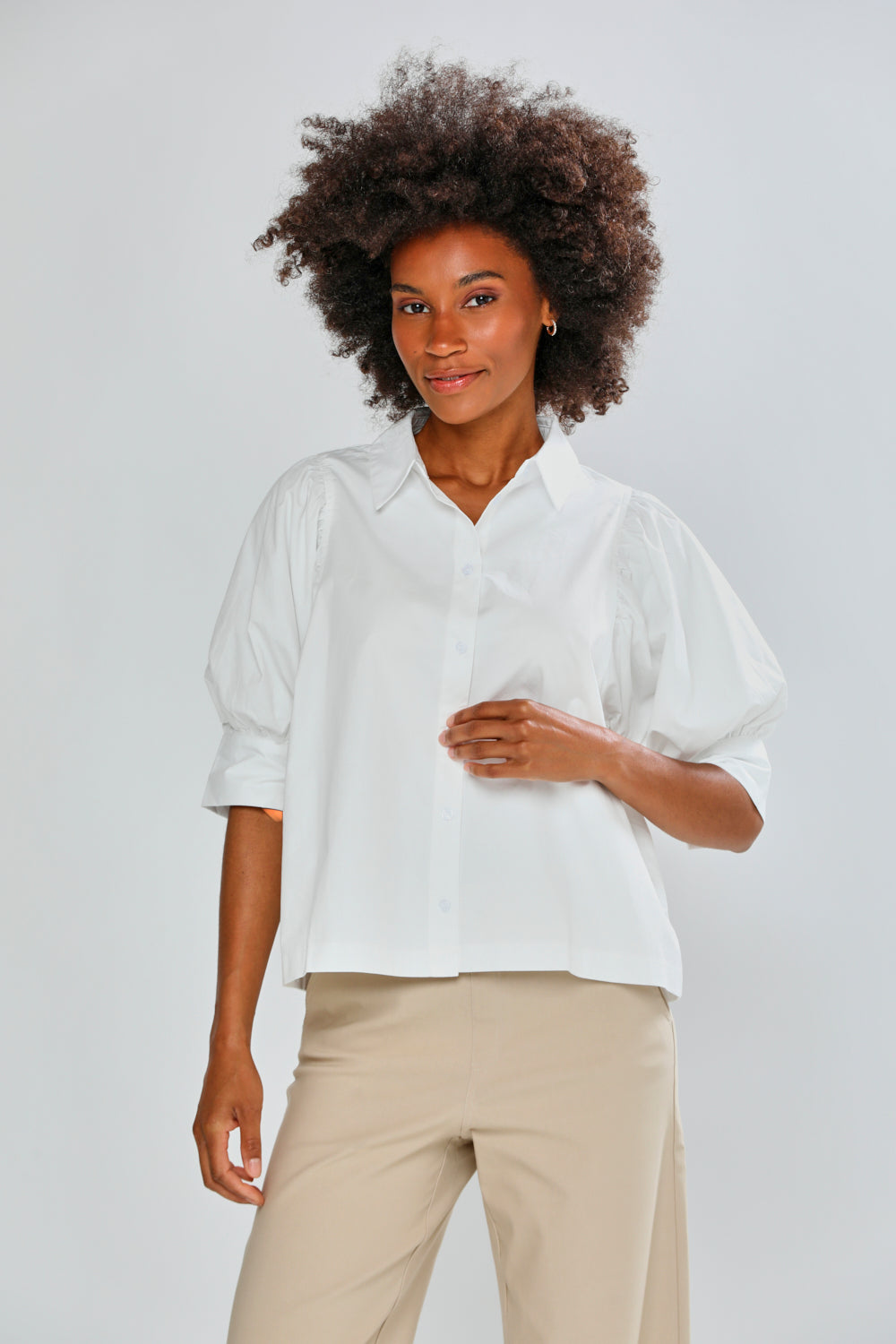 Woman wearing a white shirt and beige pants against a plain background