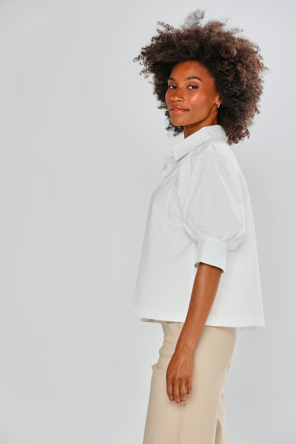 Woman wearing a white shirt and beige pants against a plain background