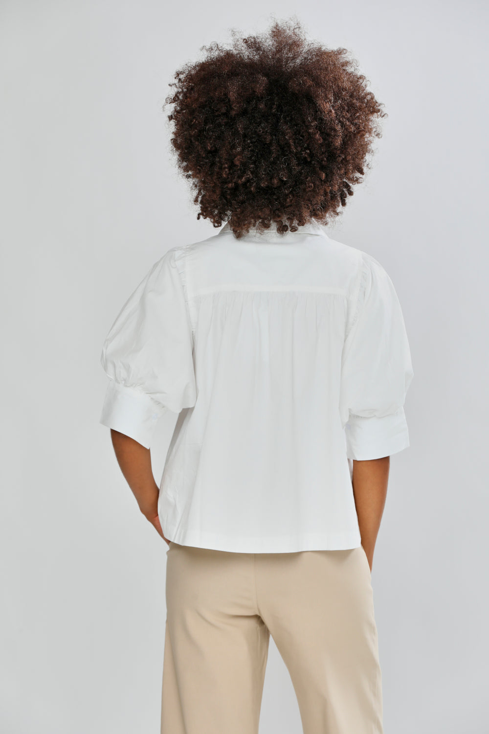 Person wearing a white blouse and beige pants against a light gray background