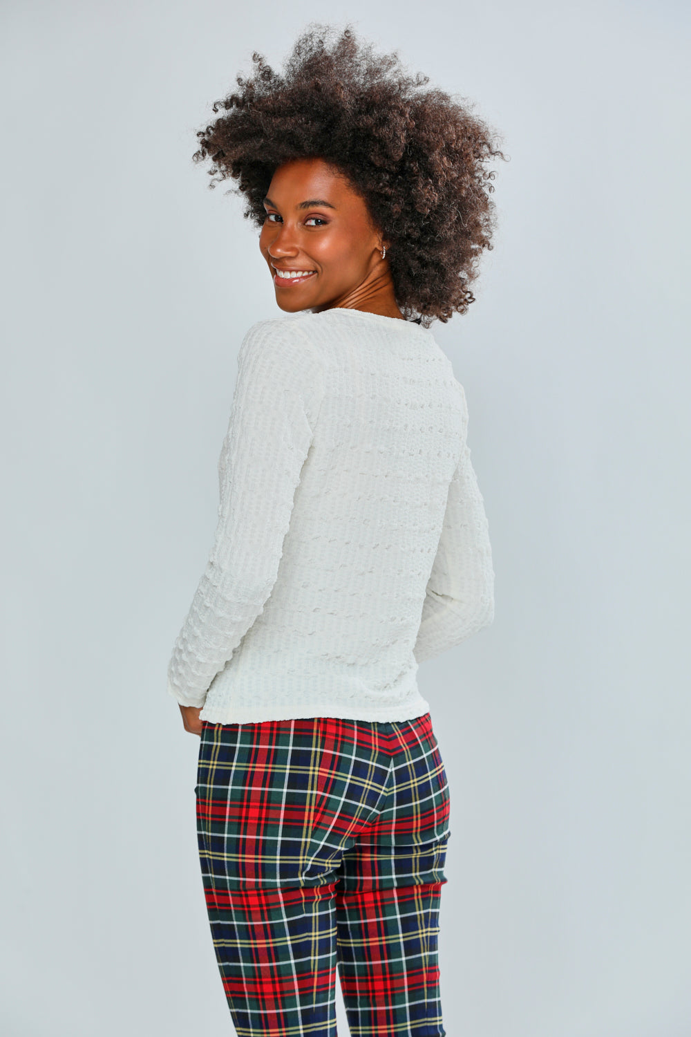 Woman wearing a white top and plaid pants on a plain background