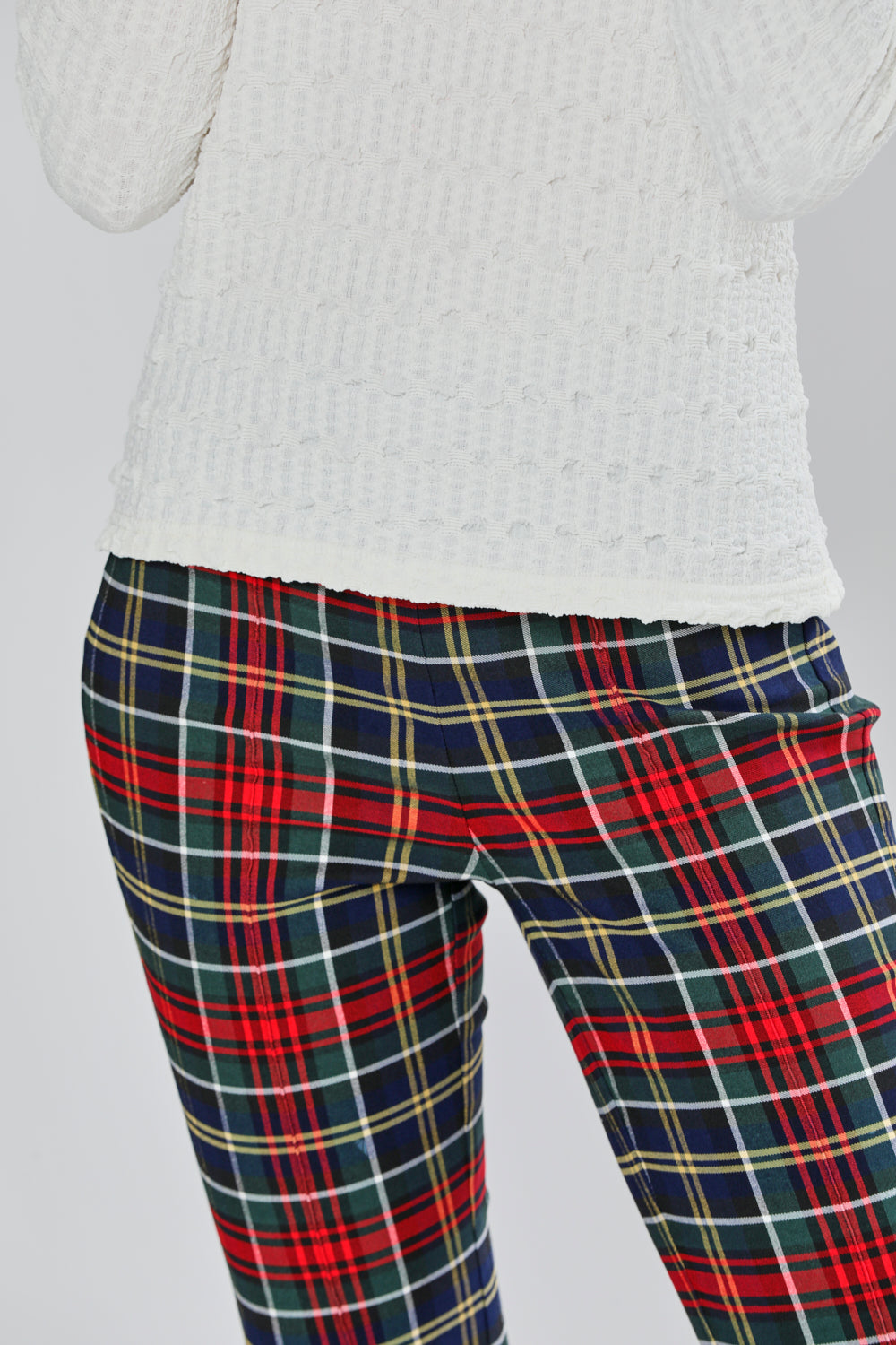 Plaid pants worn with a white sweater on a light gray background