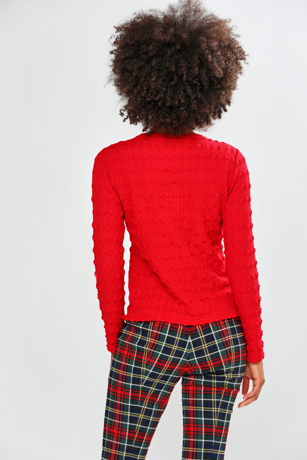 Person wearing a red textured sweater and plaid pants on a white background