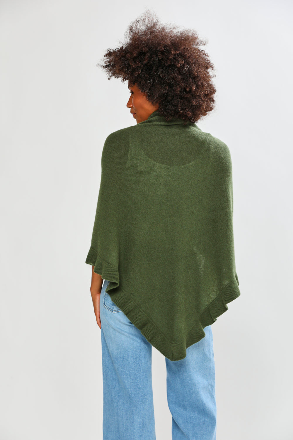 Person wearing a green poncho and light blue jeans on a white background