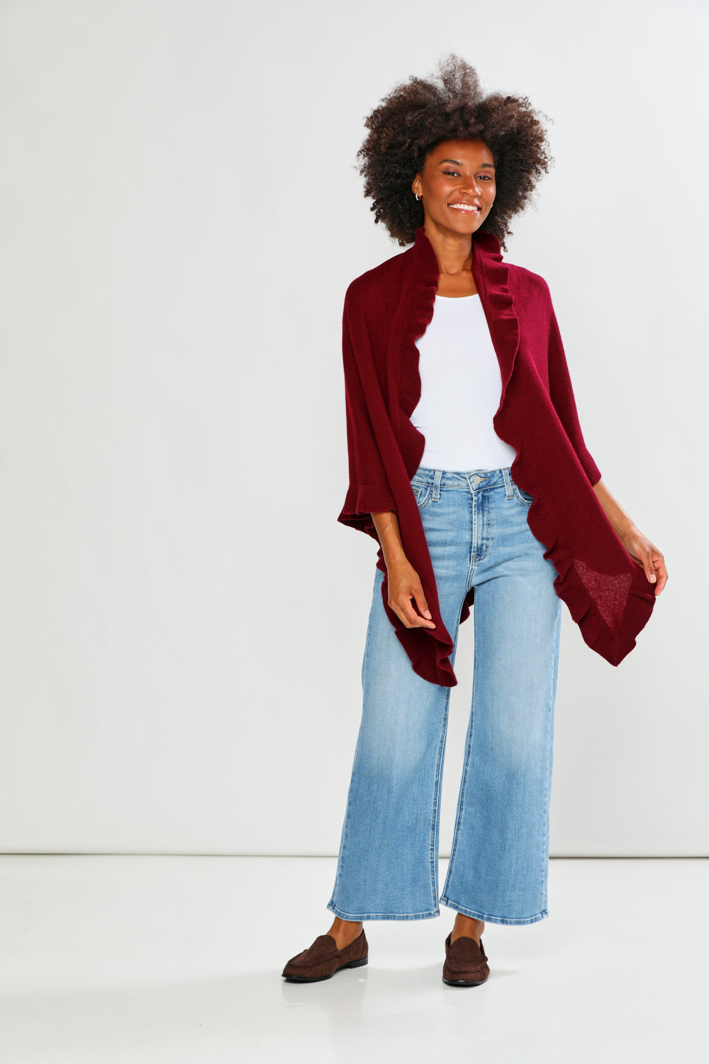 Woman wearing a burgundy cardigan, white top, and light blue jeans on a white background