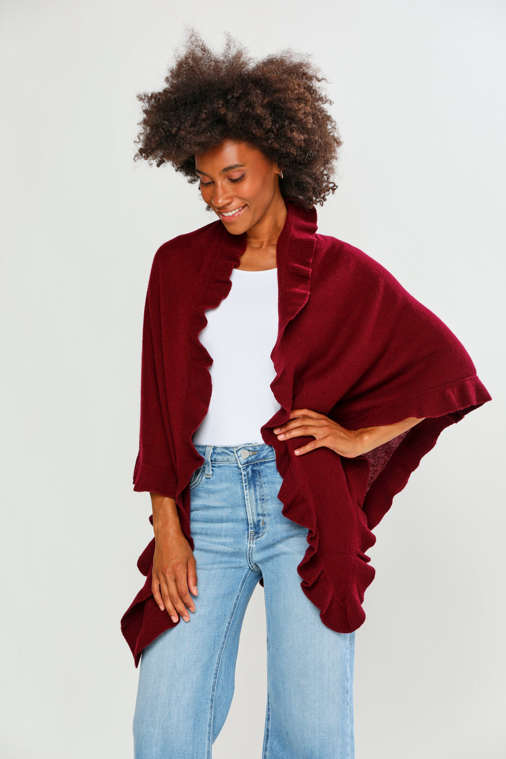 Woman wearing a burgundy shawl over a white top and blue jeans on a plain background