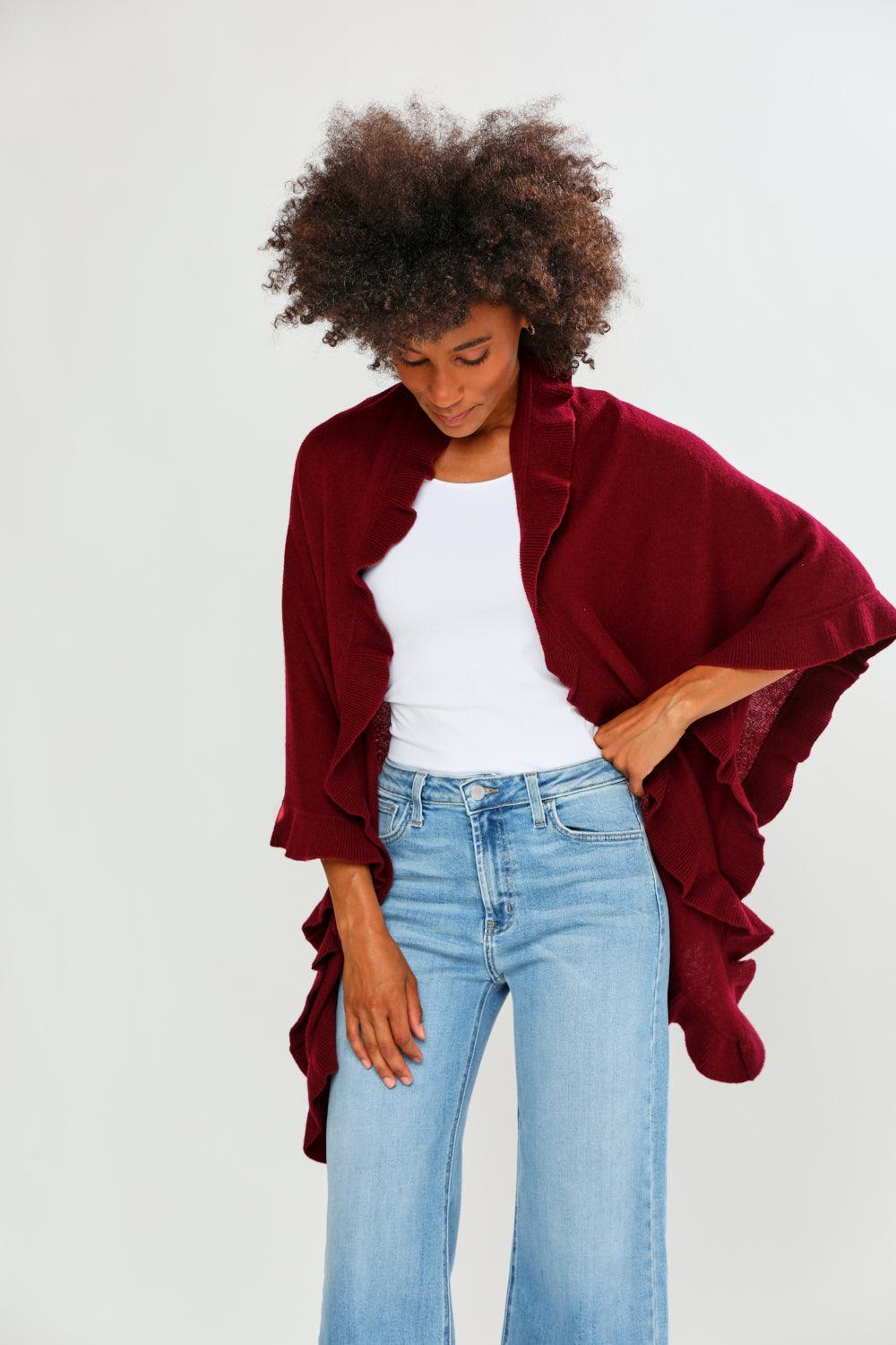 Person wearing a burgundy poncho over a white top and blue jeans on a plain background