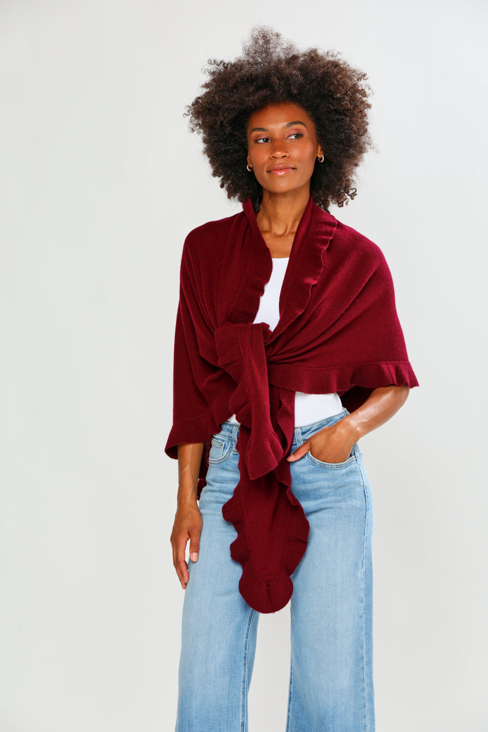 Woman wearing a burgundy shawl over a white top and blue jeans on a white background