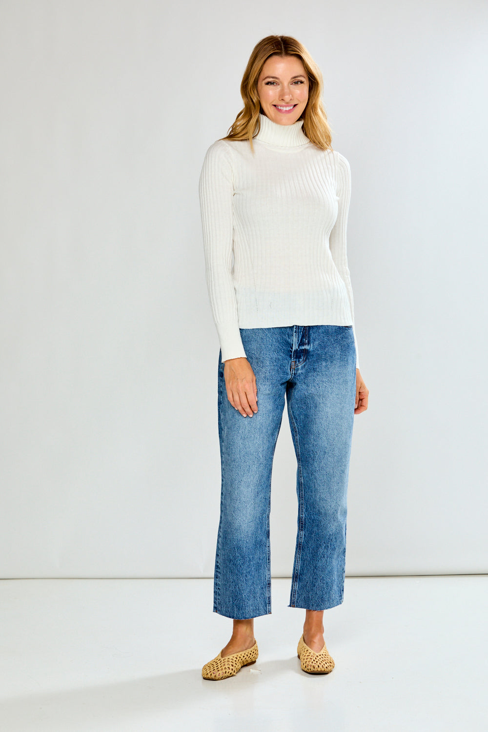 Woman wearing a white turtleneck sweater and blue jeans on a plain background