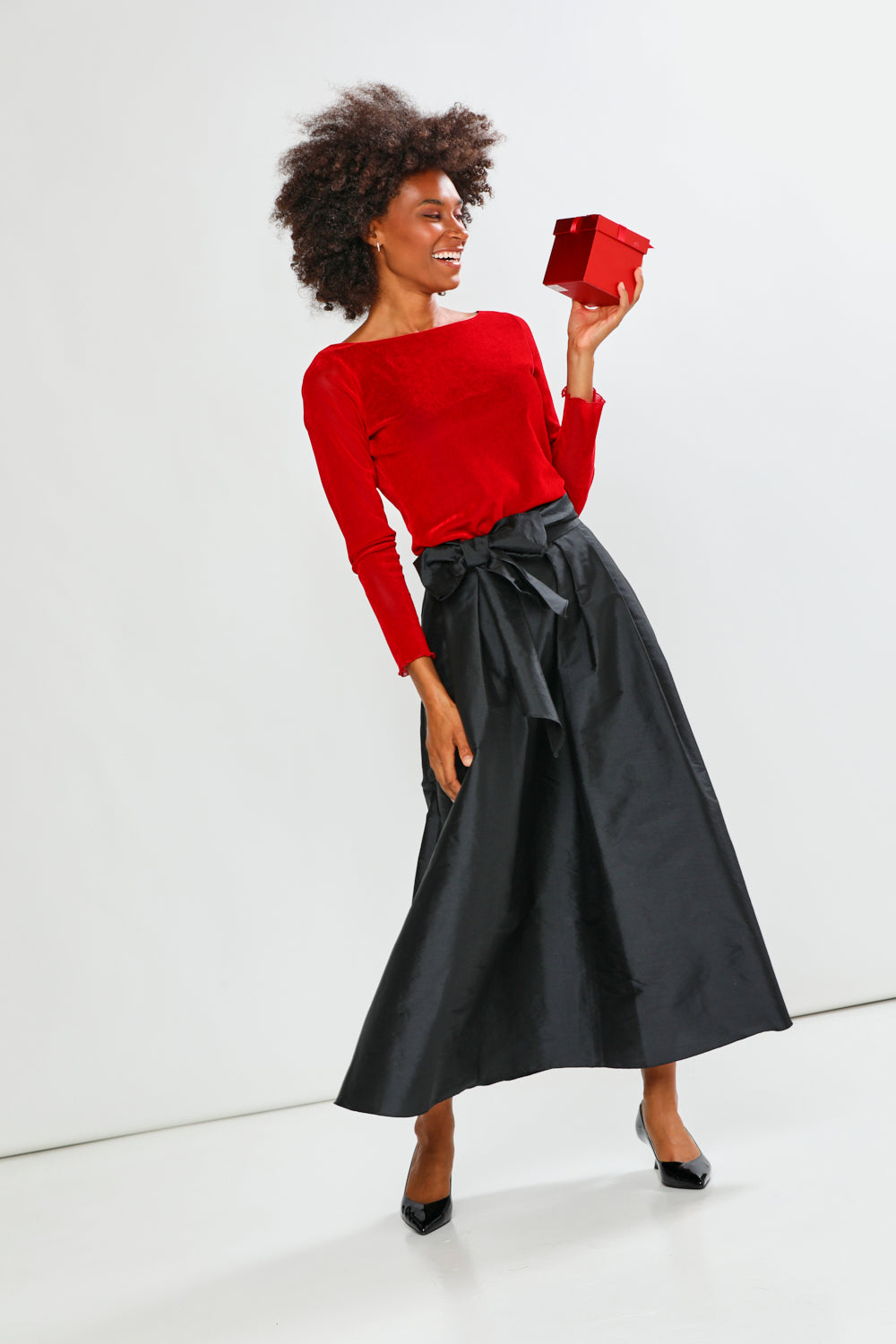 Woman wearing a red sweater and black skirt holding a red box against a white background