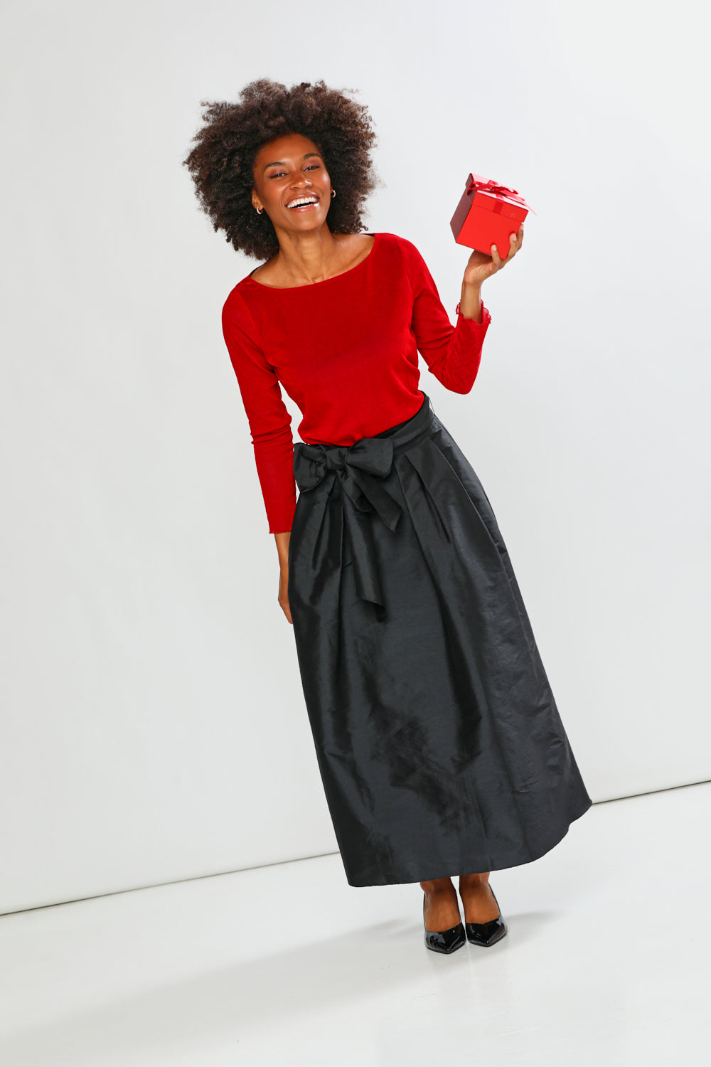 Woman wearing a red top and black skirt holding a red box against a white background