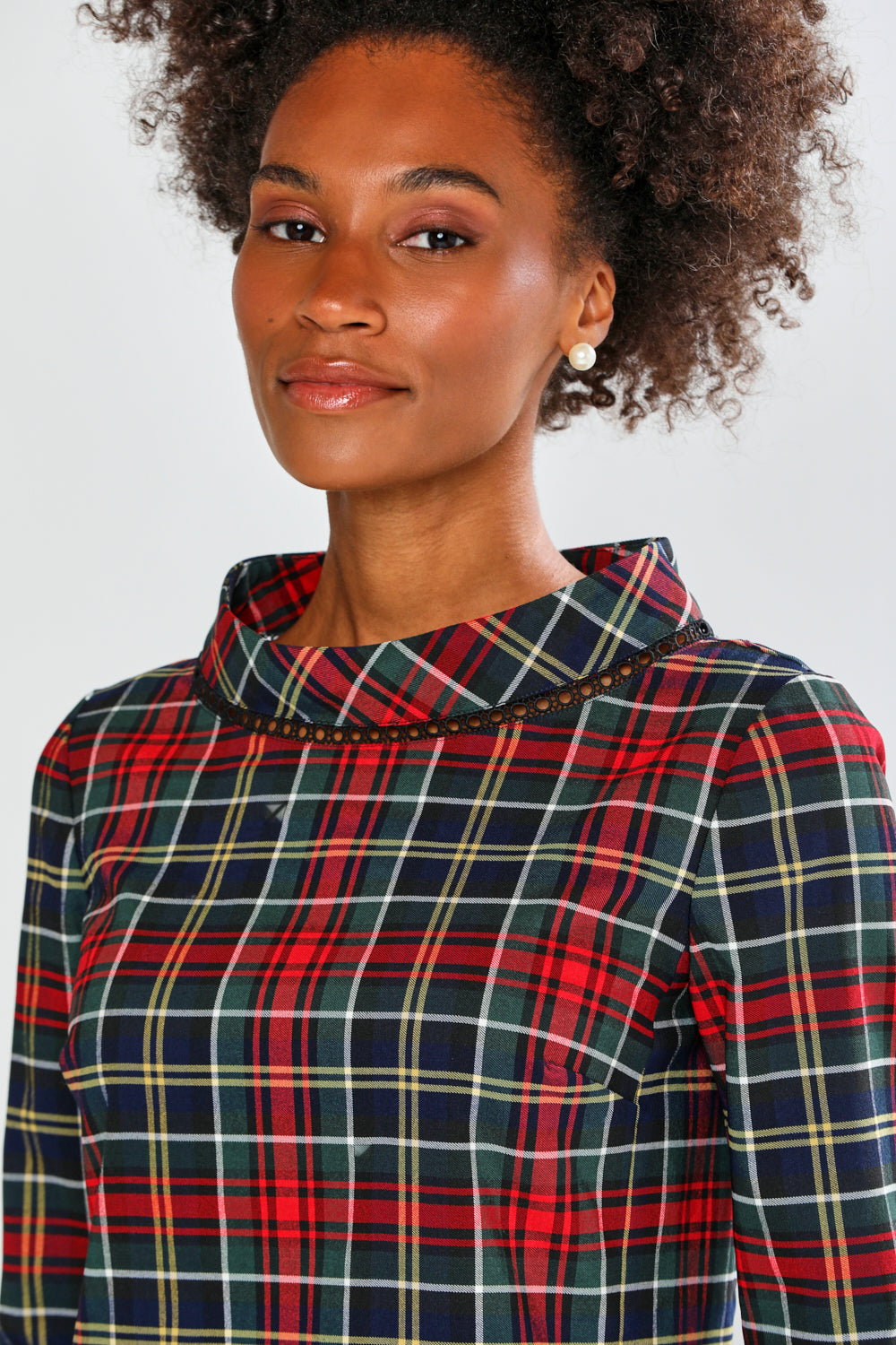 Woman wearing a red and blue plaid dress with a high collar against a white background