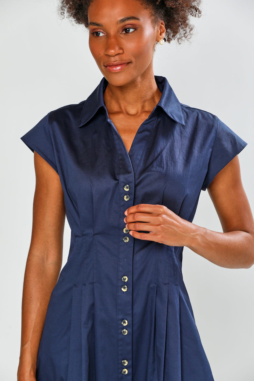 A woman wearing a navy blue short-sleeve collared shirt dress with a button-down front, shown against a light gray studio background.