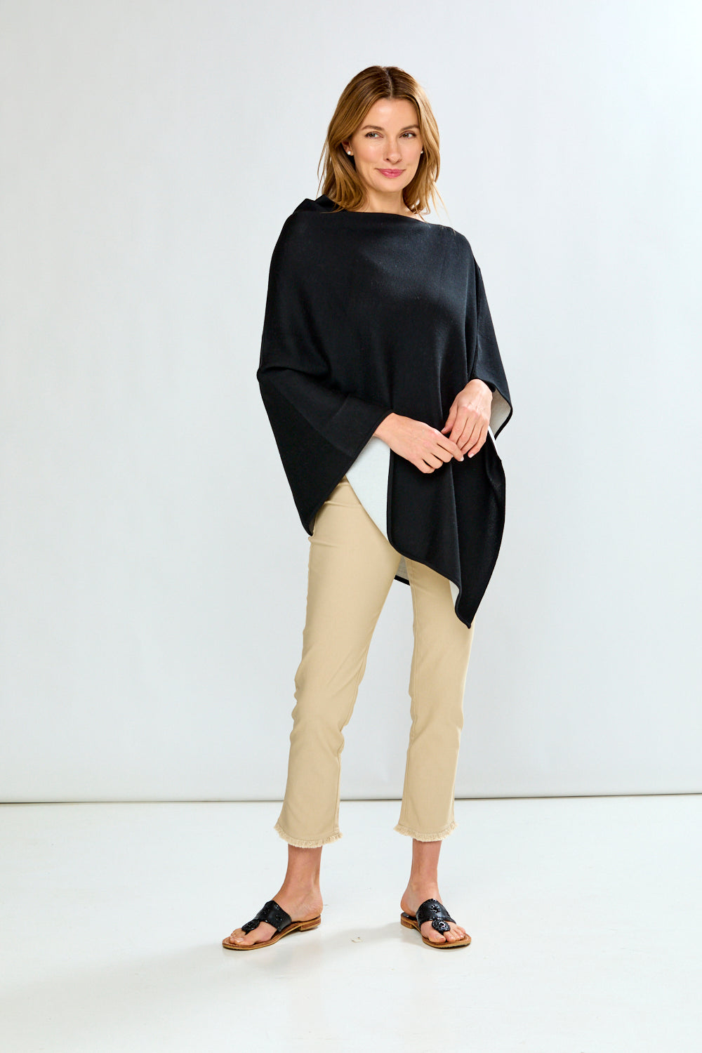 Woman wearing a black poncho and beige pants on a white background