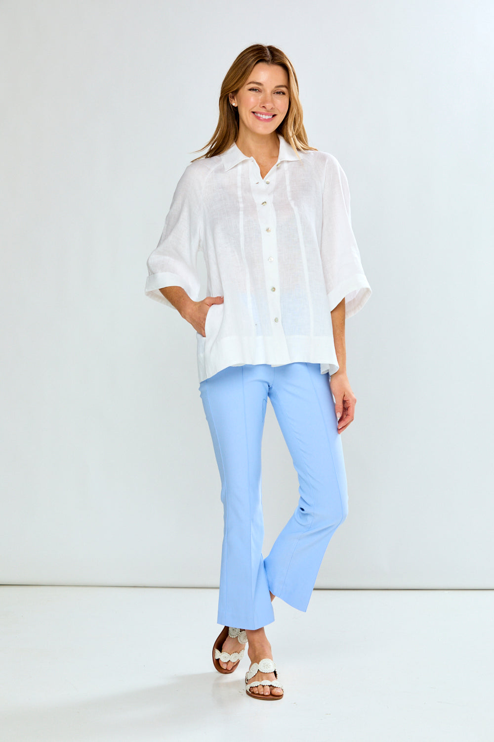 Woman wearing a white blouse and light blue pants against a white background