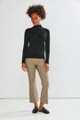 A woman modeling a black long-sleeve mock neck top and mushroom cropped trousers with black loafers, standing against a plain white studio background.