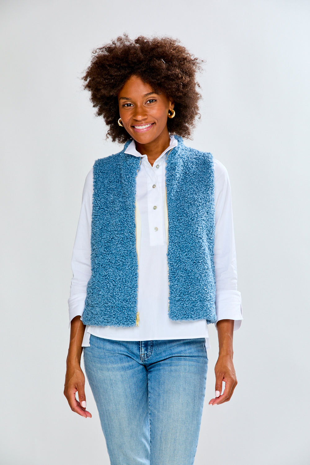 Woman wearing a blue textured vest over a white shirt and jeans on a white background