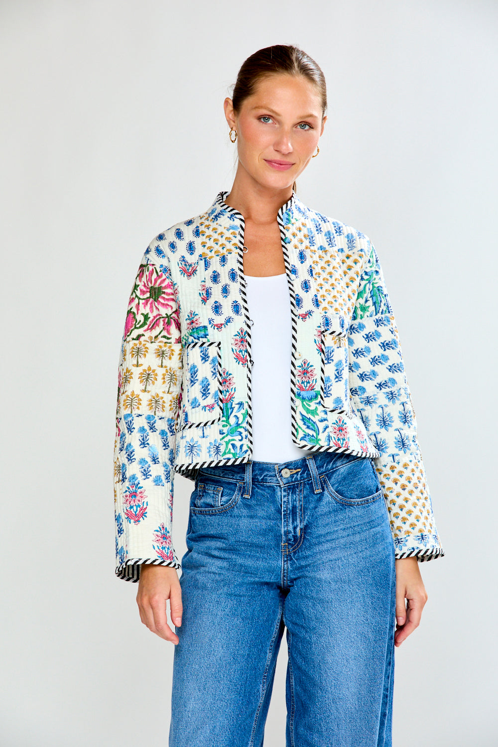 Woman wearing a colorful patterned jacket and blue jeans on a white background