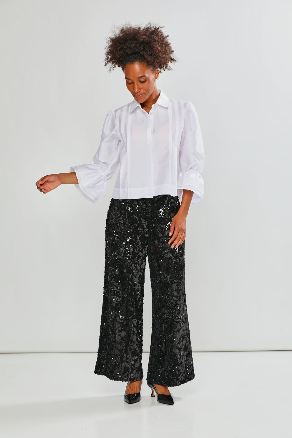 Woman wearing a white blouse and black sequin pants on a white background