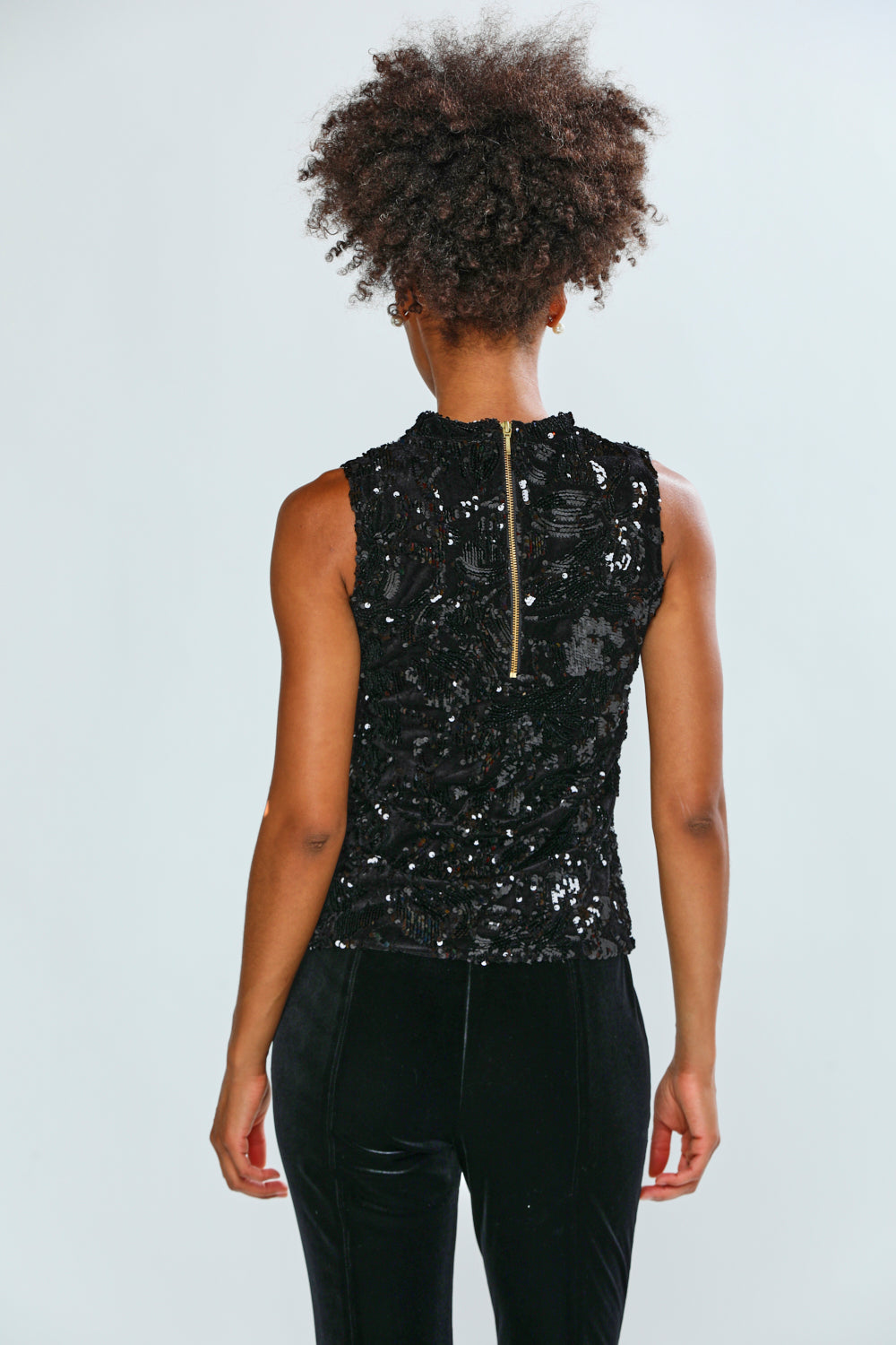 Person wearing a black sequin top and black pants on a white background