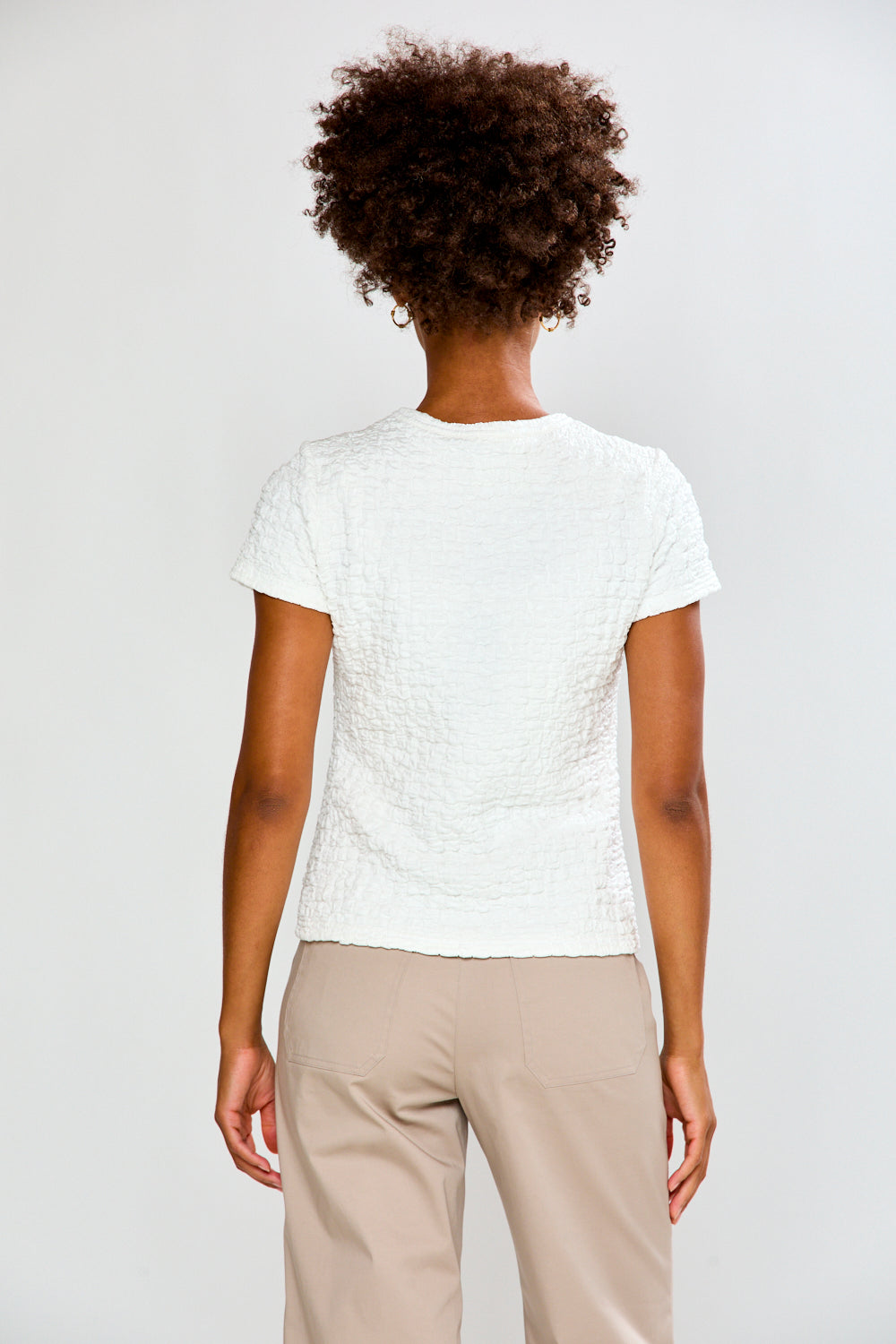 Person wearing a textured white top and beige pants on a plain background