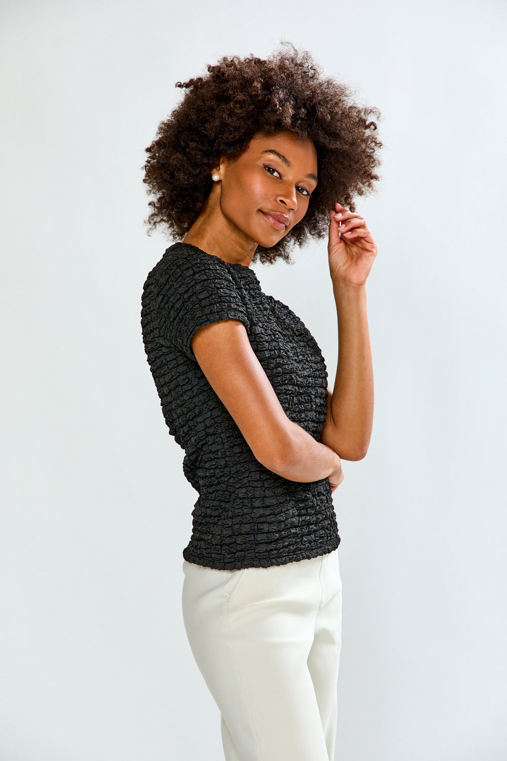 Woman wearing a textured black top and white pants against a light background
