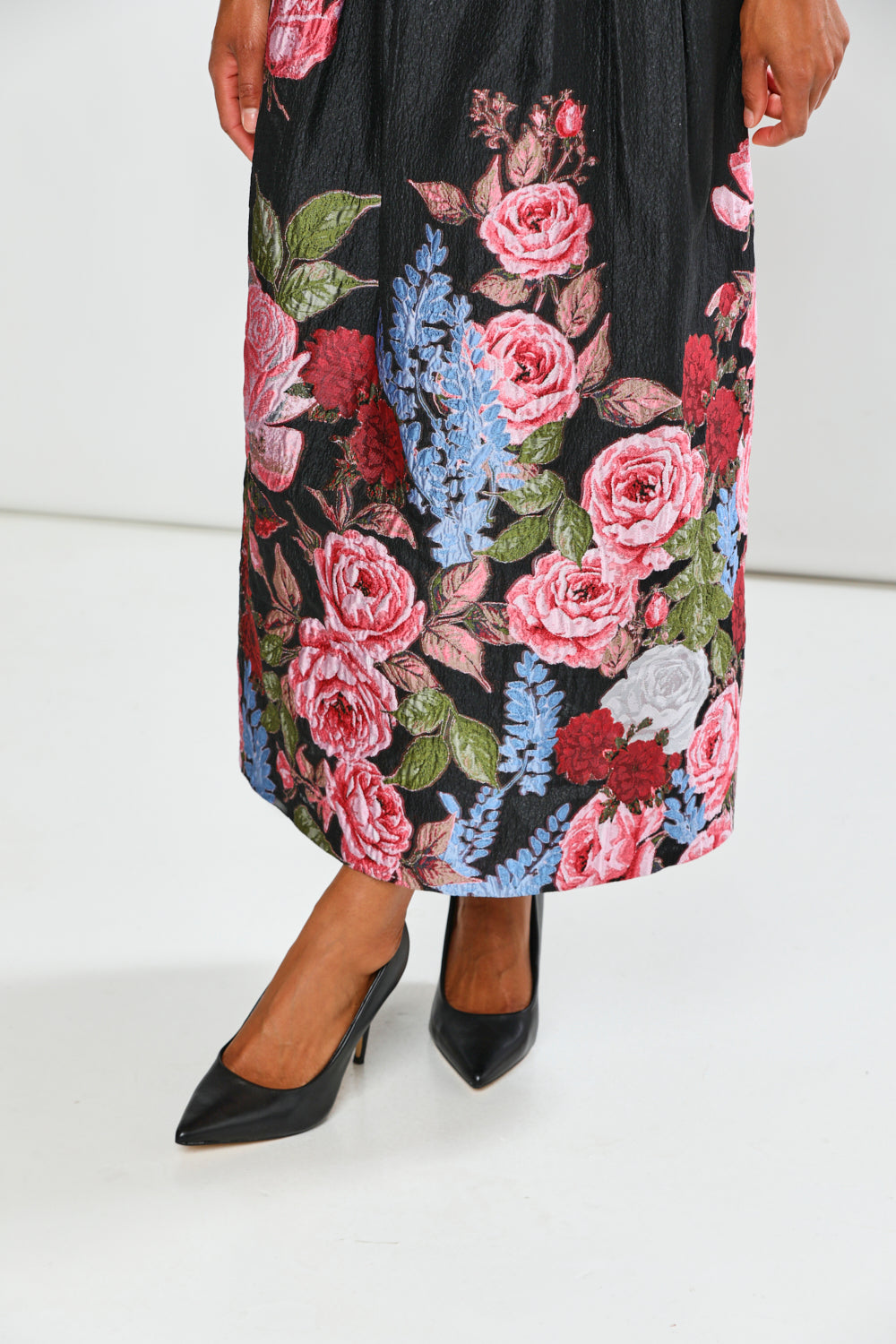 Woman wearing a black top and floral skirt on a white background