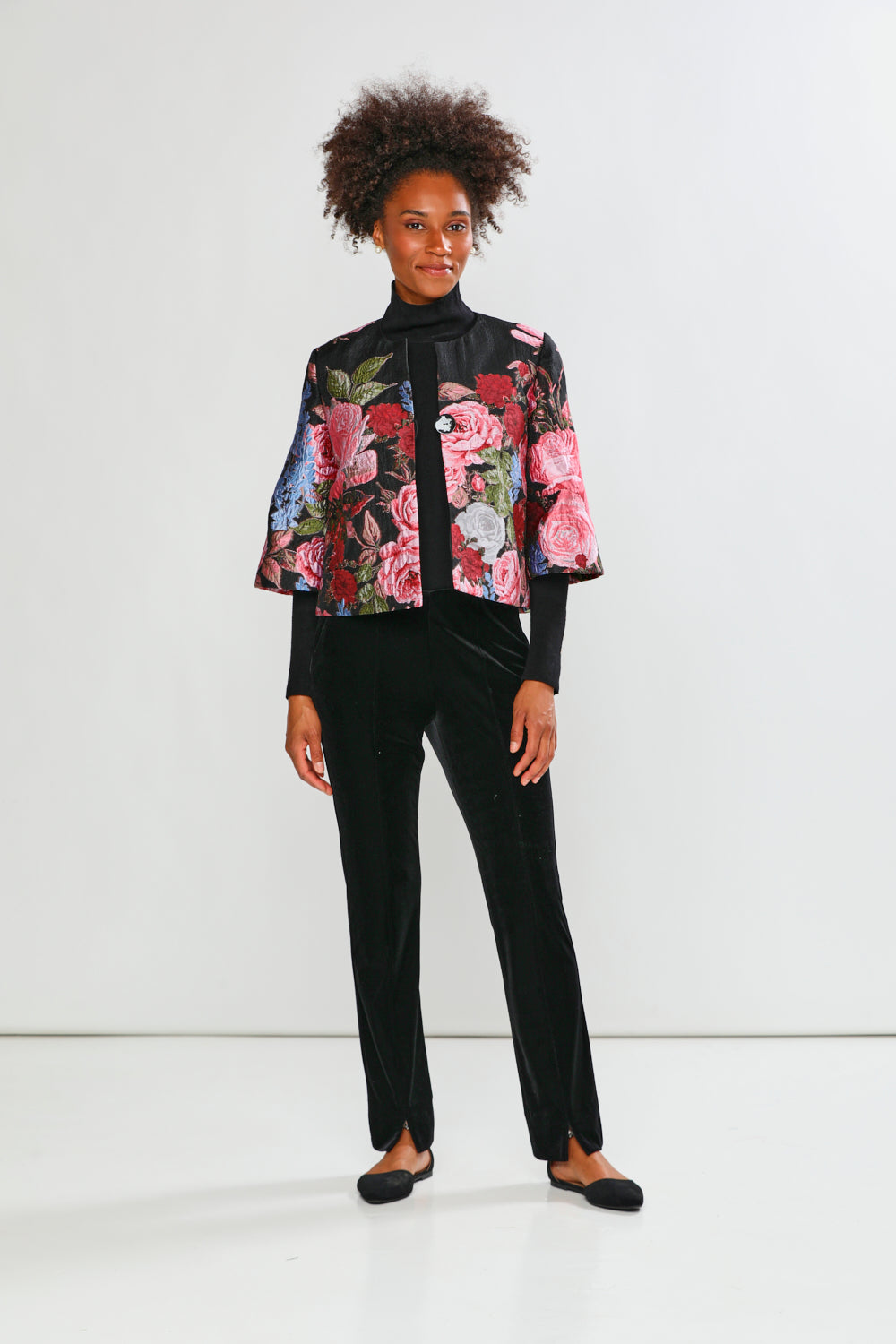Person wearing a floral embroidered jacket and black pants on a white background