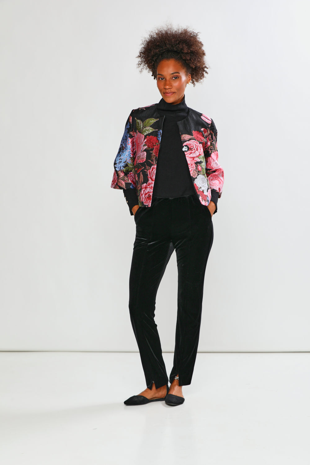 Person wearing a colorful floral jacket over a black top and pants on a white background