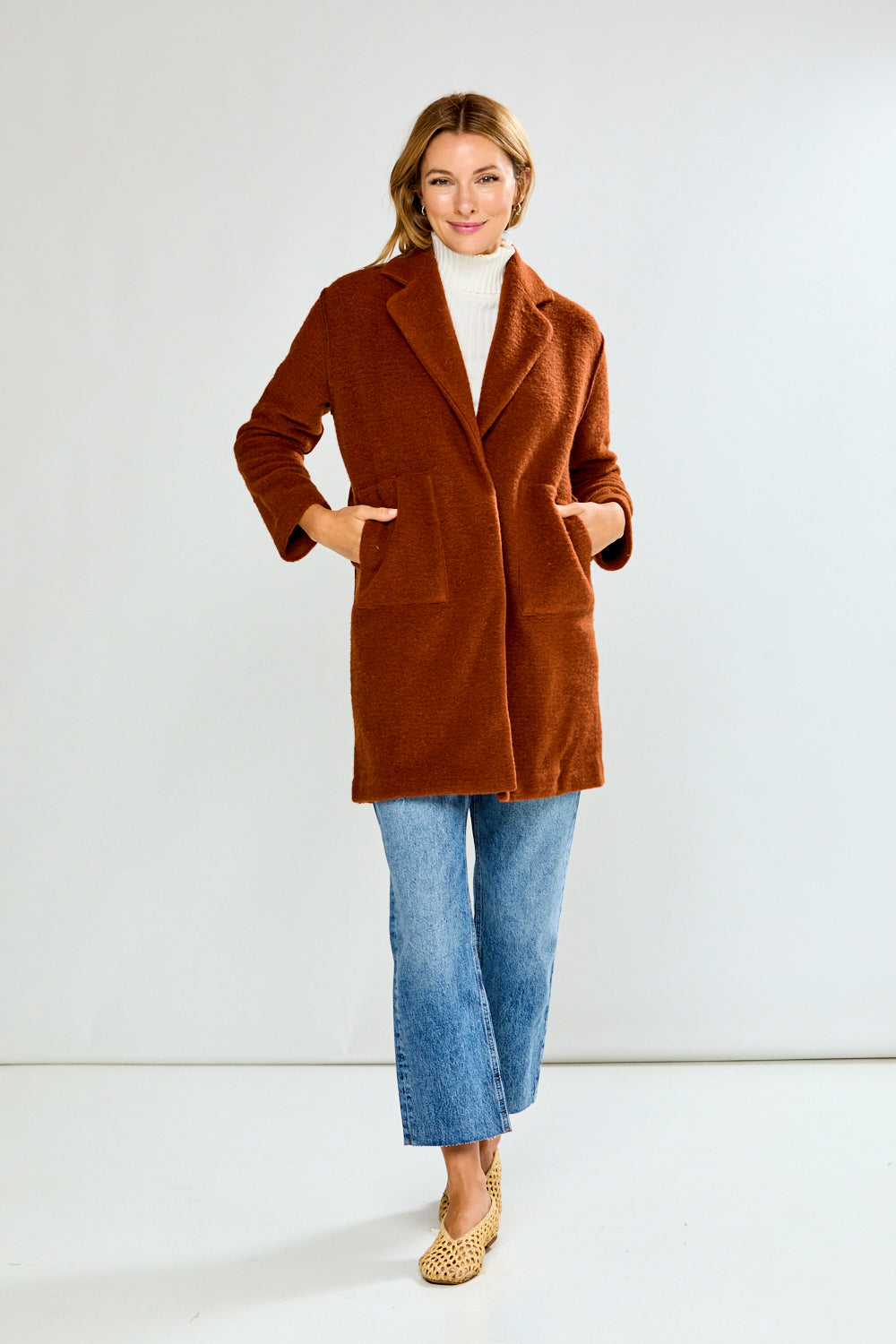 Woman wearing a brown coat over a white turtleneck on a white background