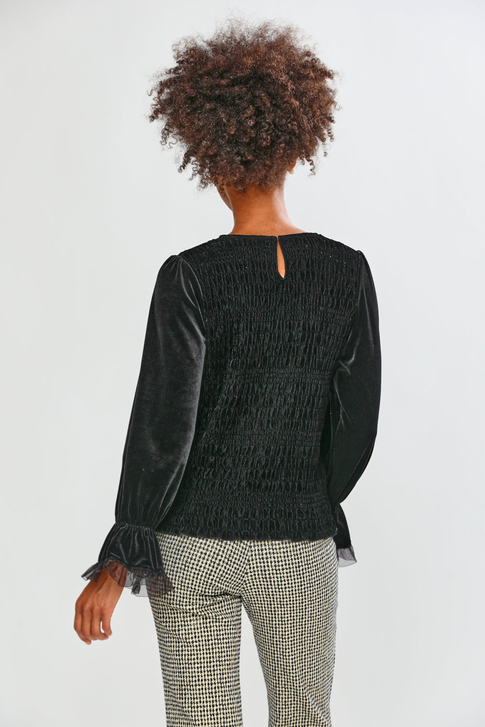 Person wearing a black textured top and patterned pants on a white background