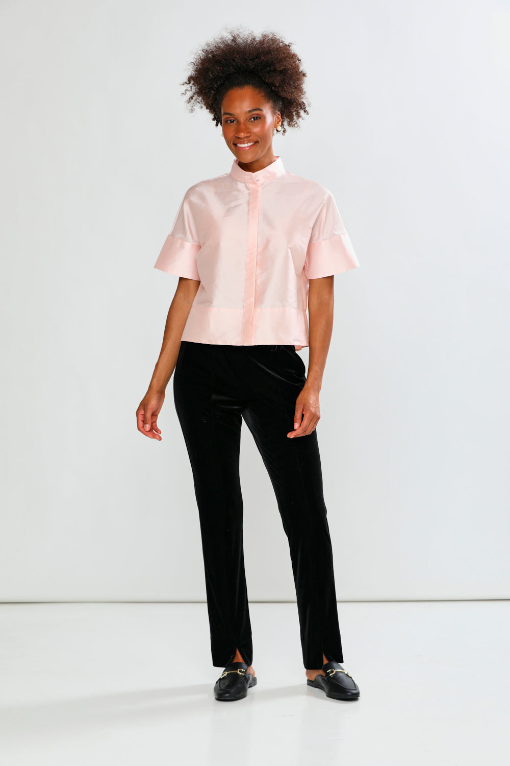 Woman wearing a light pink blouse with ruffled sleeves against a white background