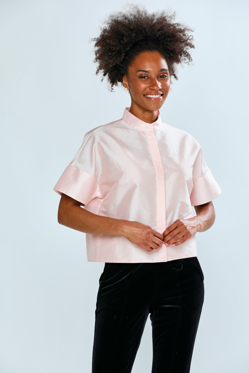 Woman wearing a light pink blouse with ruffled sleeves against a white background