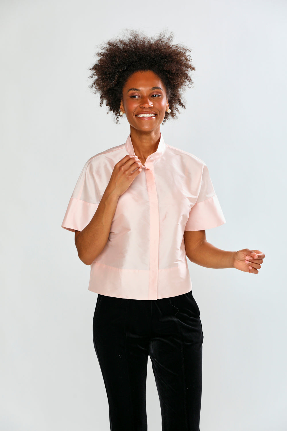 Woman wearing a light pink blouse with ruffled sleeves against a white background