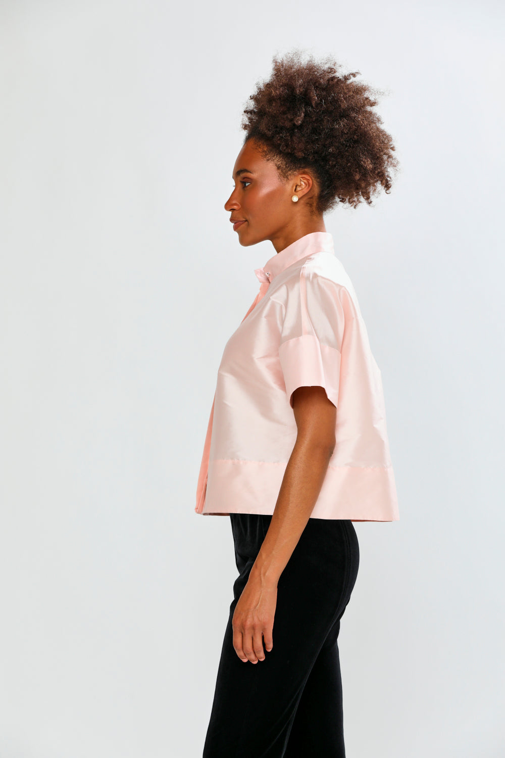 Woman wearing a light pink blouse with ruffled sleeves against a white background