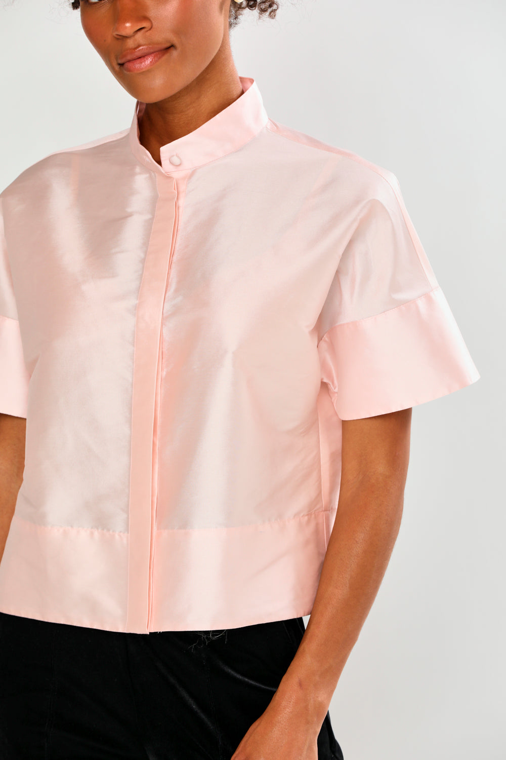 Woman wearing a light pink blouse with ruffled sleeves against a white background