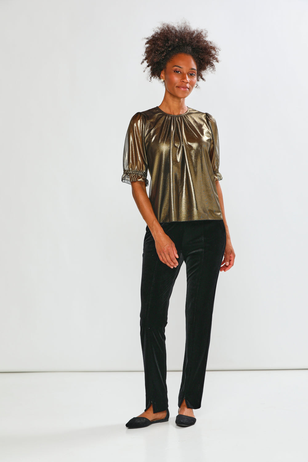Woman wearing a gold metallic top with black pants on a white background